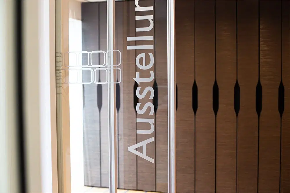 Glaswand mit vertikalem Schriftzug Ausstellung und braunen Holzpaneelen im Hintergrund