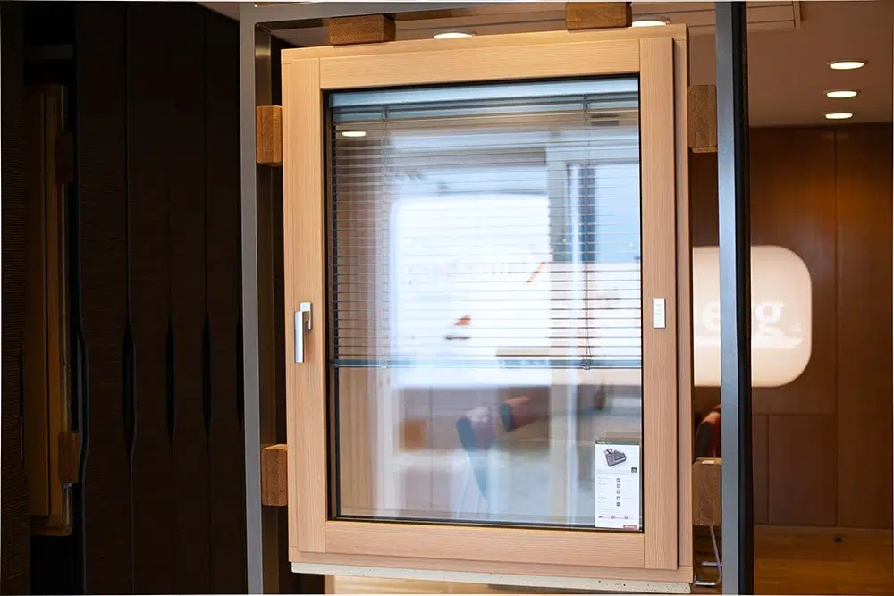 Fenster mit hellem Holzrahmen und integrierter Jalousie in einem Ausstellungsraum