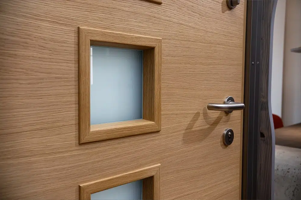 Helle Innentür aus Holz mit zwei quadratischen satinierten Glaseinsätzen, Edelstahl-Türgriff und Schließzylinder.