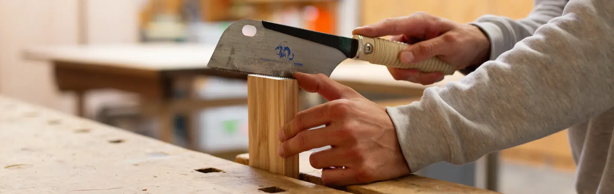 Auszubildender in einer Werkstatt sägt ein kleines Holzstück mit einer Feinsäge auf einer Werkbank.