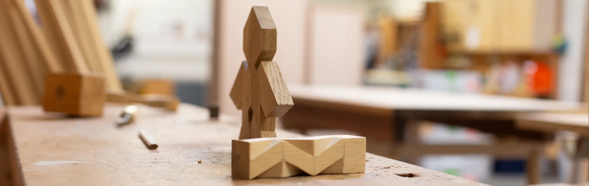 Kleine geschnitzte Holzfigur und Werkstück auf einer Werkbank in einer Tischler-Ausbildungswerkstatt.