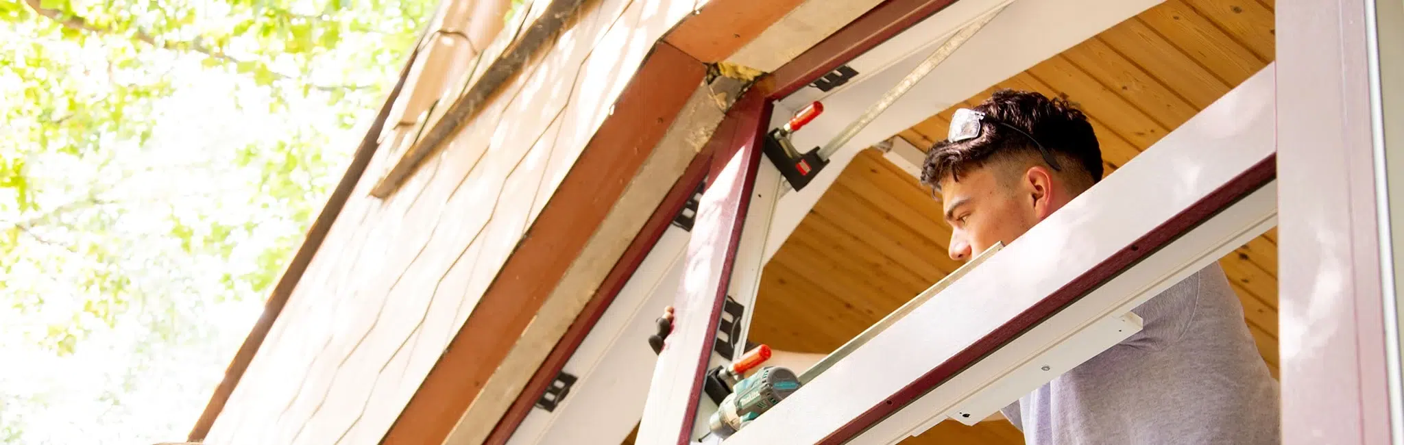 Handwerker montiert einen Fensterrahmen in einer Hausöffnung, dabei sind Bohrmaschine und Spannzwingen sichtbar