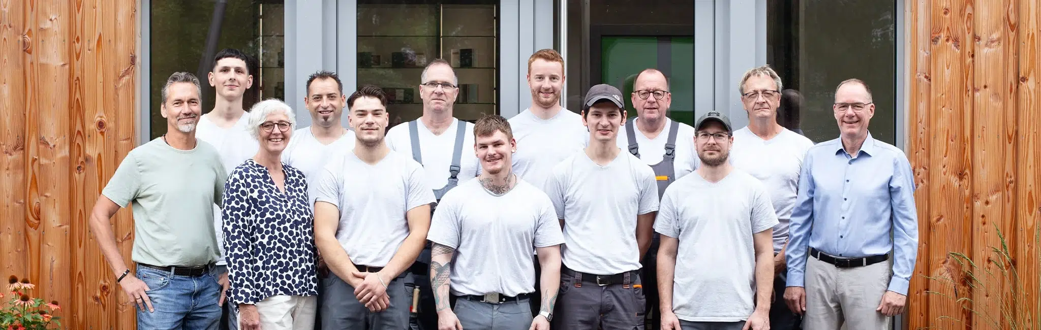 Teamfoto des Klauenberg-Teams mit mehreren Mitarbeitenden in Arbeitskleidung vor dem Firmengebäude mit Holzfassade.